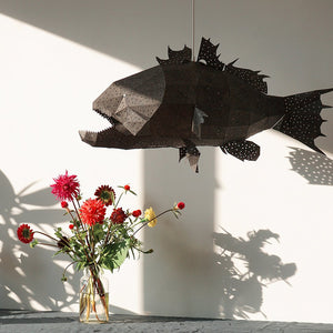 A black fish-shaped Nautical Ceiling Lamp hanging above a table next to a vase with red flowers in it.