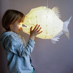A little boy is joyfully holding up a Nautical Hanging Light Glowfish in a Kids' Room.