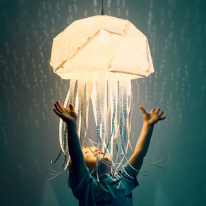 A child is holding up a Vasili Lights Nautical Hanging Jellyfish Light designed for a Child's Room or Nursery.