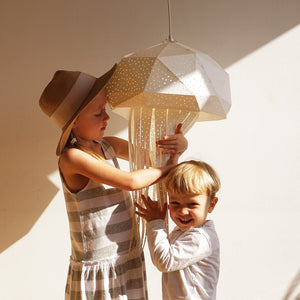 Two young children are holding the Nautical Hanging Jellyfish Light, mesmerizing origami art lamp made of paper-like fabric.