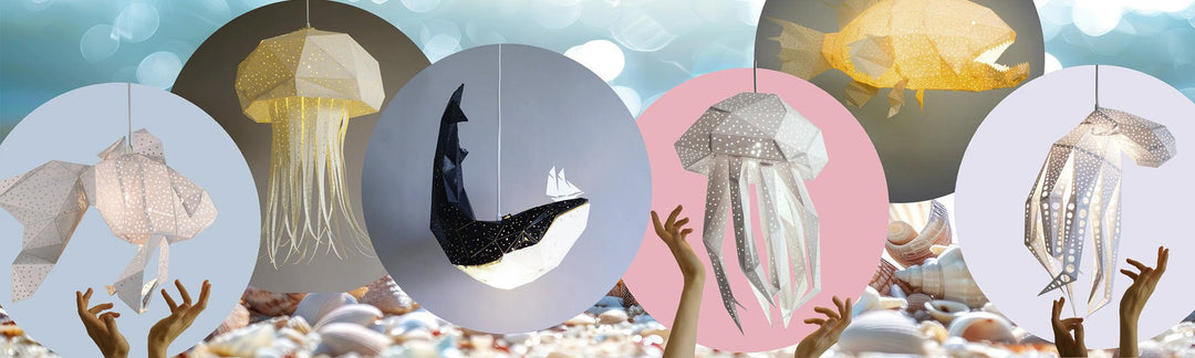 Paper jellyfish, whale and fish pendant lights hanging in colored circles above children's hands reaching up from a pebble seabed