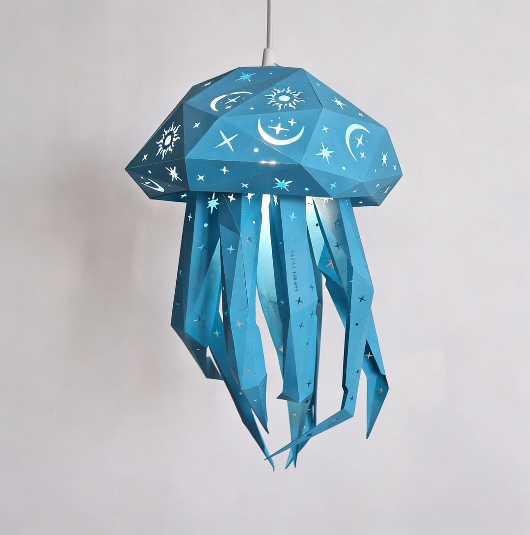 A blue jellyfish-shaped pendant light with a faceted starry sky pattern, hanging against a plain light gray wall.