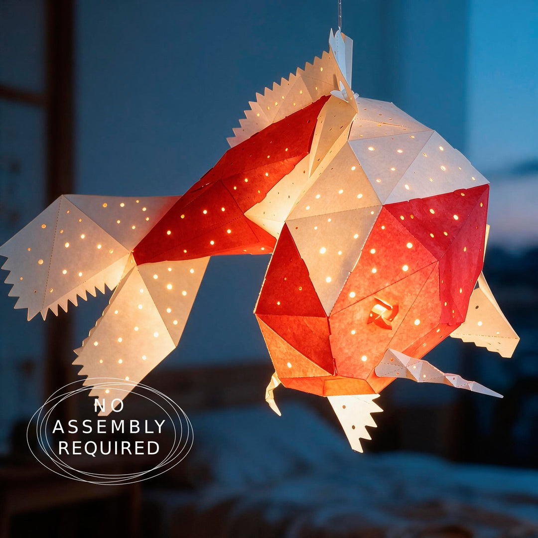 A geometric origami-style fish lantern hanging in a dimly lit room, glowing with warm light through cutout sections. White and red paper panels form the fish shape.