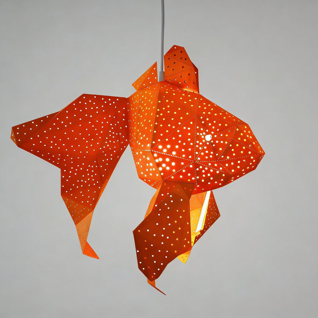 The Bubble Goldfish Lamp by Vasili Lights, a DIY paper night light kit designed for nurseries, children's rooms, and bedrooms, features an orange goldfish lantern shape with perforated holes that let light shine through, suspended against a plain gray background.