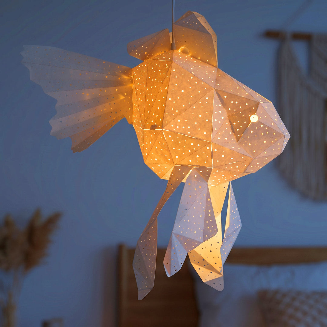 A lit White Goldfish Origami Pendant Light in a dim blue room