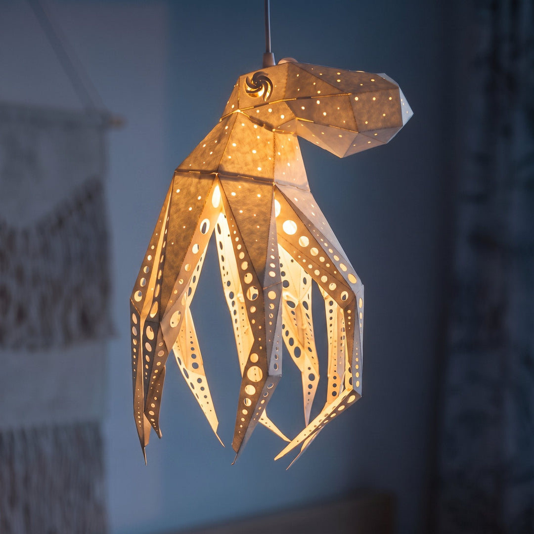 A lit White Octavio the Octopus Pendant Light in a blue room with a wall hanging