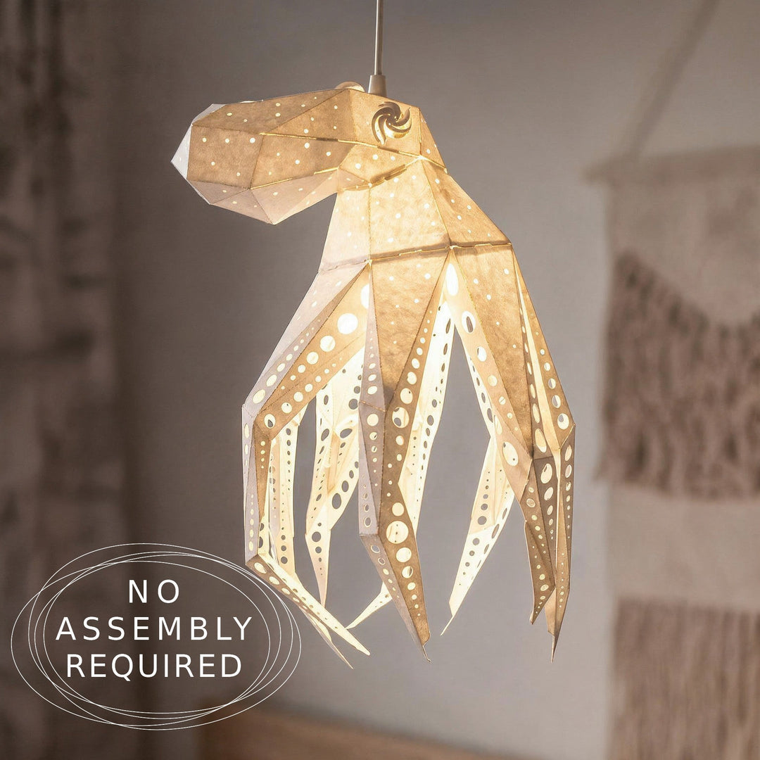 A hanging octopus-shaped paper lantern light with a warm glowing interior, shown against a softly blurred indoor background. A circular badge in the lower left reads 'NO ASSEMBLY REQUIRED'.