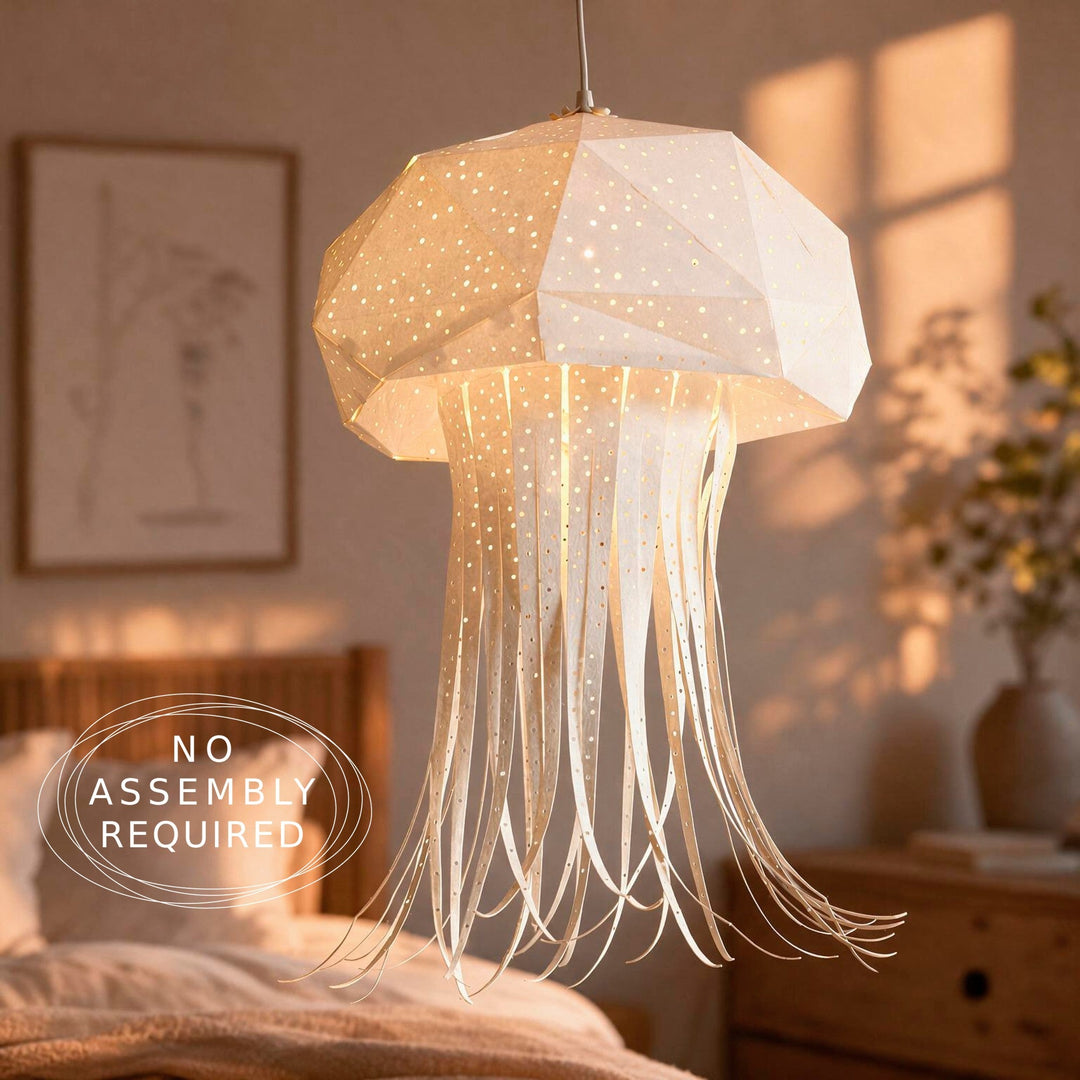 A jellyfish-shaped hanging pendant lamp with a faceted translucent shade and long flowing strands, shown in a softly lit bedroom. The lamp glows warm white.