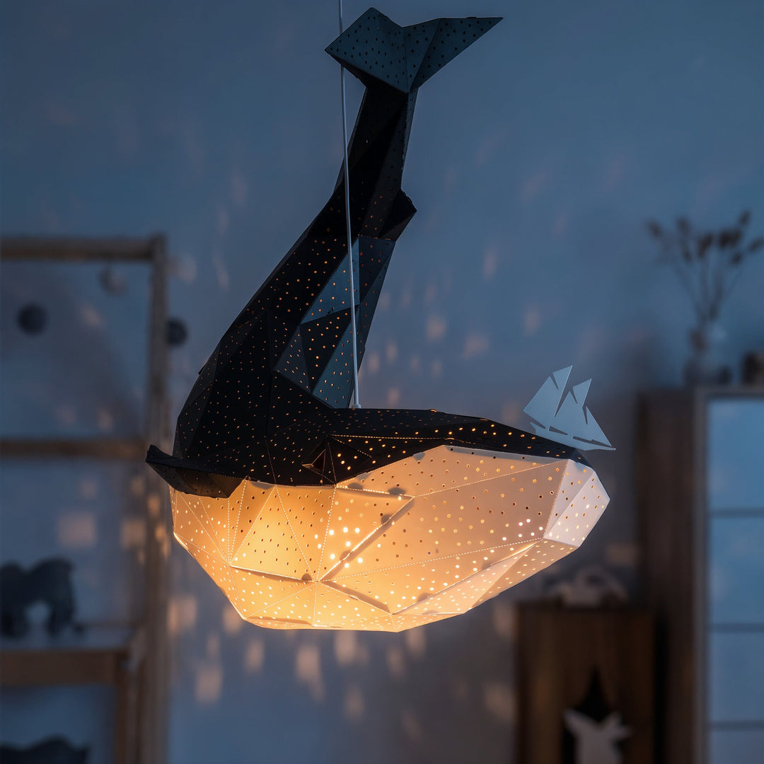 A lit Black-White Origami Whale Pendant Light in a dim blue room