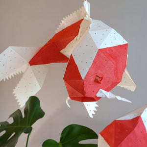 A pair of Koi Kohaku Light I origami fish sitting on top of a plant, made by VASILI LIGHTS.