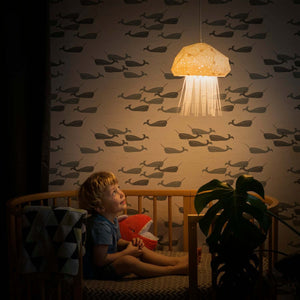 An Jelly Lamp shaped as jellyfish hangs above a child sitting in a crib in his Nursery.