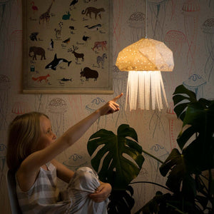 A cute girl is pointing to Jelly Lamp shaped as a jellyfish, hanging in her room.