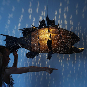 A cute girl igirl playing with a black fish-shaped Nautical Ceiling Lamp casting light patterns on the blue wall.