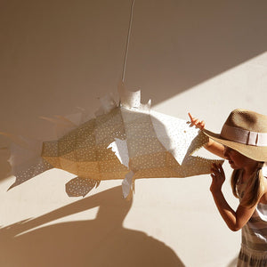 A cute girl in a hat is holding a white fish-shaped Nautical Ceiling Lamp casting dark shadows on the white wall.