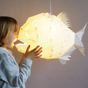 A whimsical Nautical Hanging Light Glowfish is being held up by a little boy in a children's room.